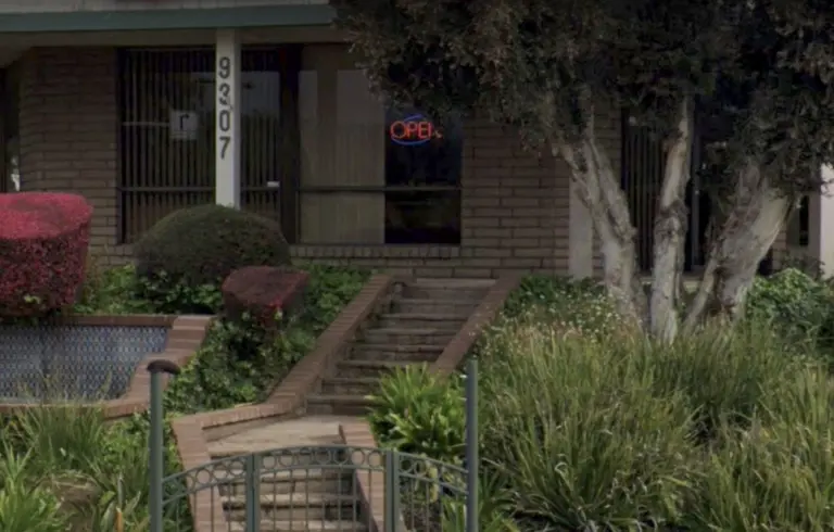 The front of the office at 9307 Carlton Hills Blvd: a brick building with the number 9307 on a white post, a red OPEN sign in the window, and brick steps climbing through a garden from a small iron gate